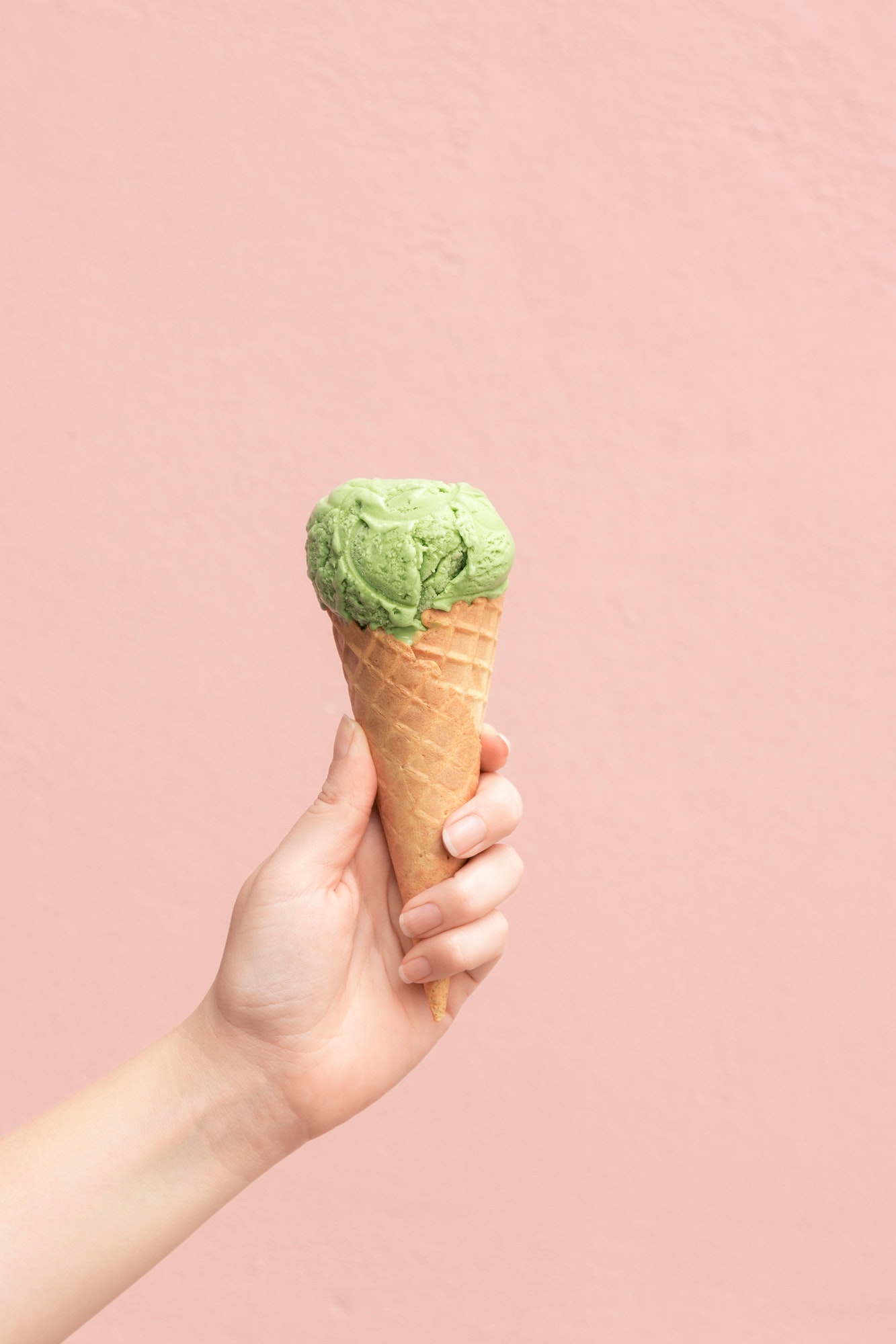 woman-holding-a-matcha-ice-cream-cone-against-a-pink-wall.jpg